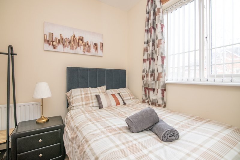Bedroom with double bed, patterned bedding, dark headboard, and large window with curtains