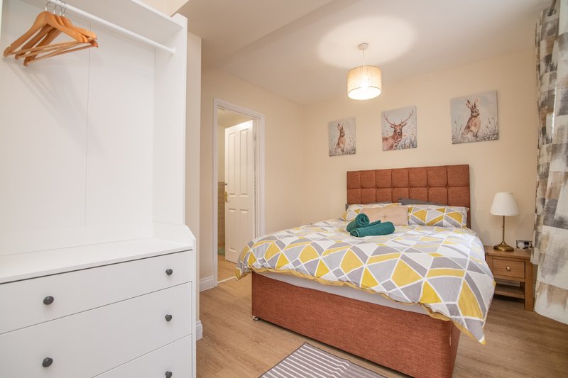 Bedroom with double bed, terracotta headboard, white dresser, wooden nightstands and warm lighting