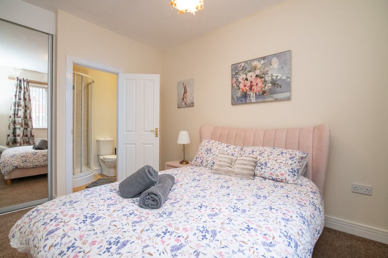 Bedroom with double bed, pink headboard, floral bedding, and ensuite bathroom visible