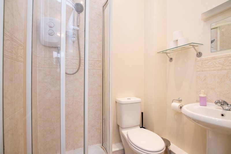 Clean bathroom with shower cubicle, toilet, sink and beige tile walls