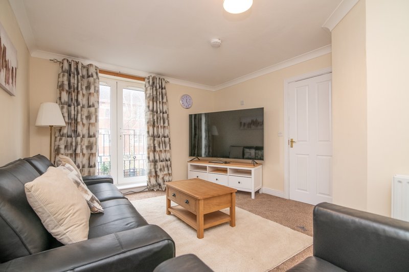 Spacious living room with dark leather sofas, wooden coffee table, wall-mounted TV and patterned curtains