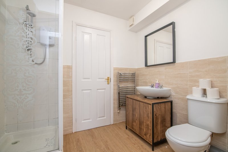 Modern bathroom with shower enclosure, wooden vanity, toilet, and heated towel rail