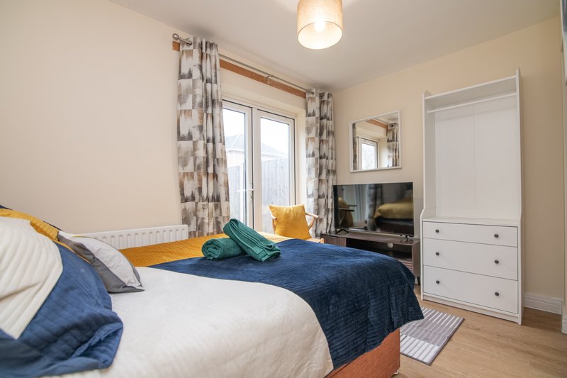 Bright bedroom with double bed, white furniture, patterned curtains and wall mirror