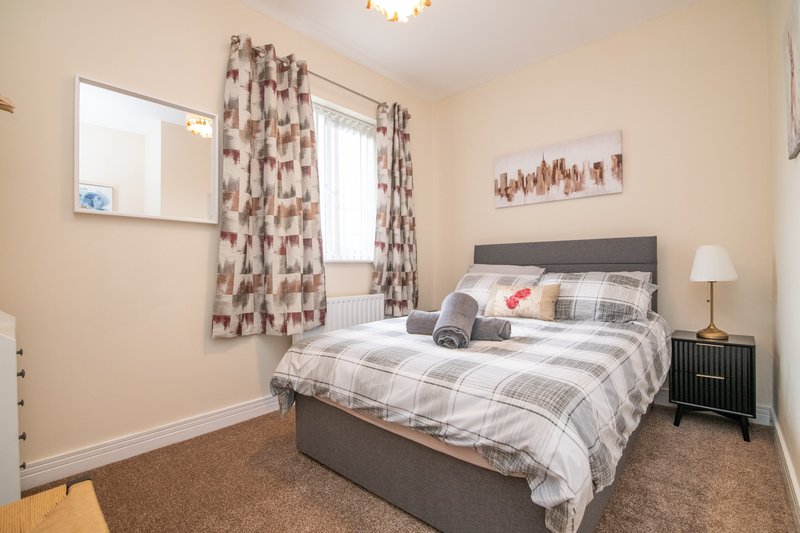 Bedroom with double bed, grey headboard, patterned curtains, mirror and bedside lamp