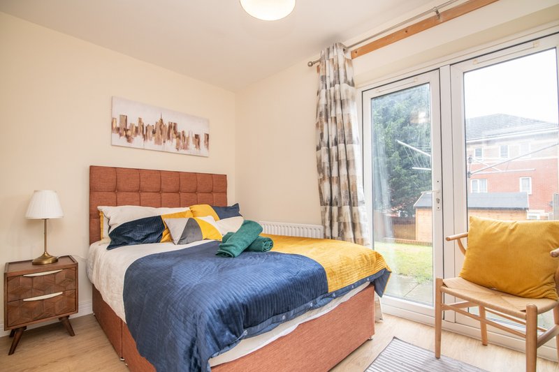 Bright bedroom with double bed, wooden furniture, colorful cushions and garden view