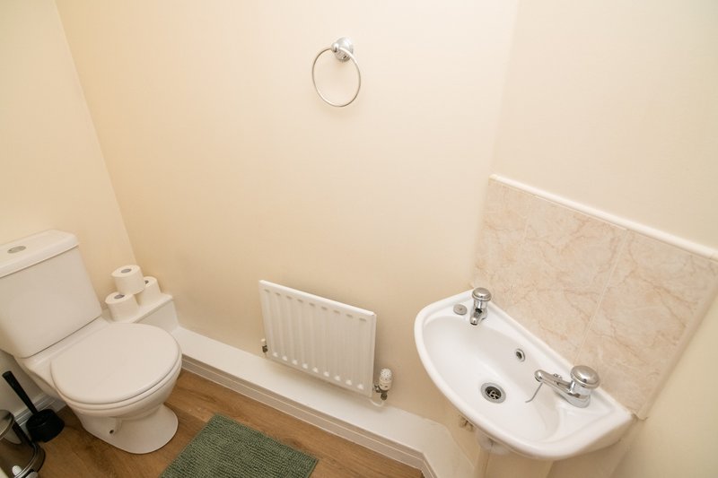 Compact bathroom with toilet, sink, radiator, and cream-colored walls