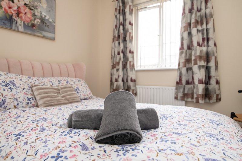 Bedroom with pink headboard, patterned bedding, rolled towel, window with patterned curtains