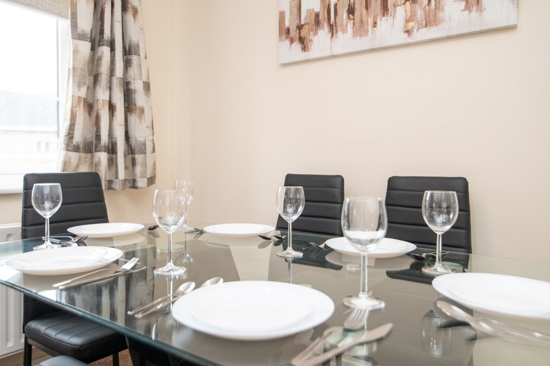 Modern dining room with glass table, black chairs, place settings and window with patterned curtains