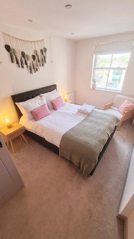 Bright bedroom with double bed, pink pillows, wooden headboard and window with natural light