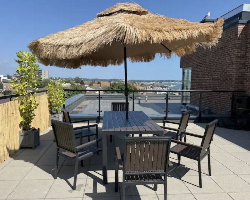 Rooftop terrace with thatched umbrella, dining table, chairs and city views