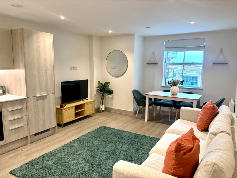 Modern open-plan living room with cream sofa, wooden TV unit, desk area, and city views