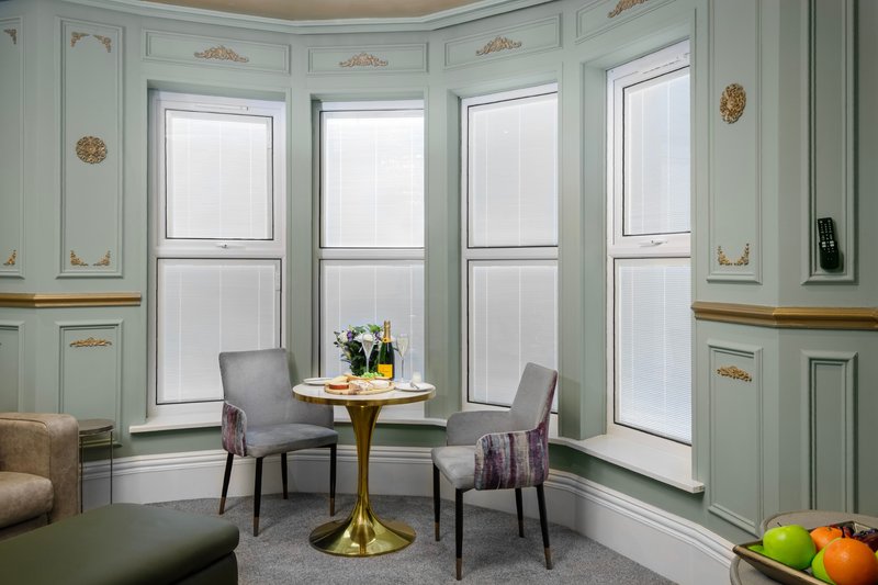 Elegant sitting area with two grey chairs, round brass table, and large multi-pane windows