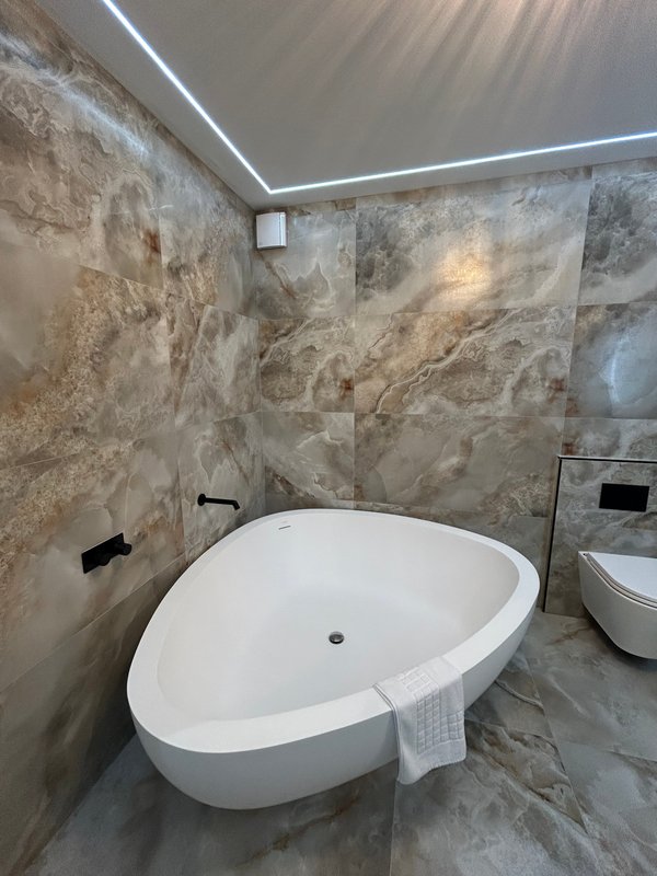 Modern bathroom with freestanding white oval bathtub, marble-effect tile walls and LED ceiling lighting