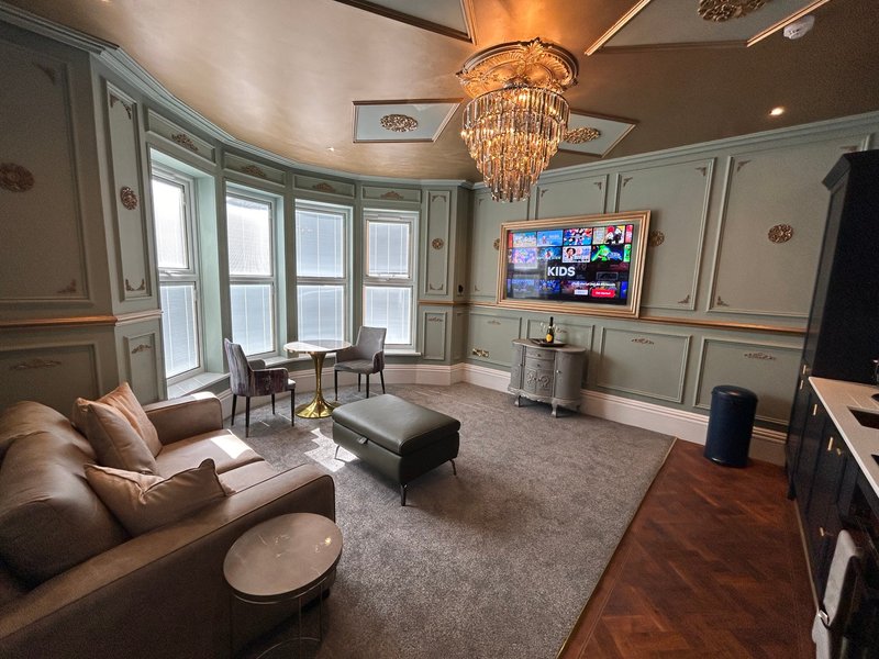 Luxury living room with curved sofa, chandelier, wall-mounted TV, and large windows