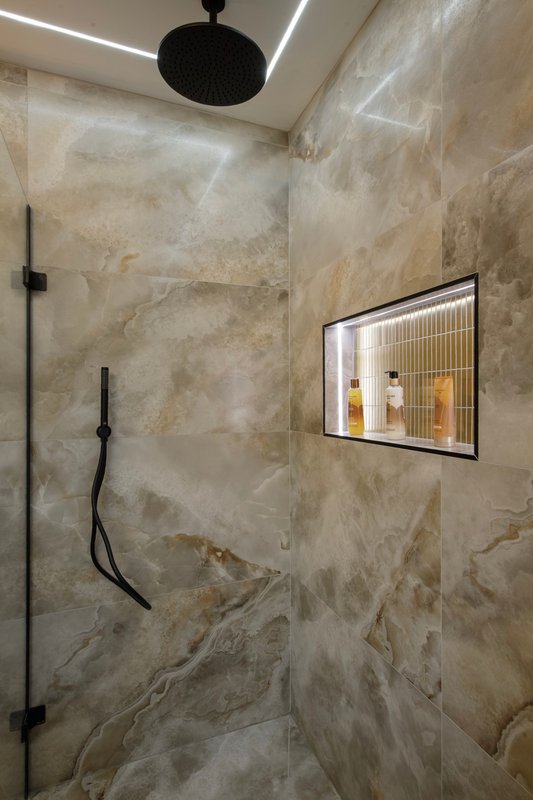 Modern bathroom with marble-effect tiled walls, rainfall showerhead, black fixtures and illuminated mirror cabinet