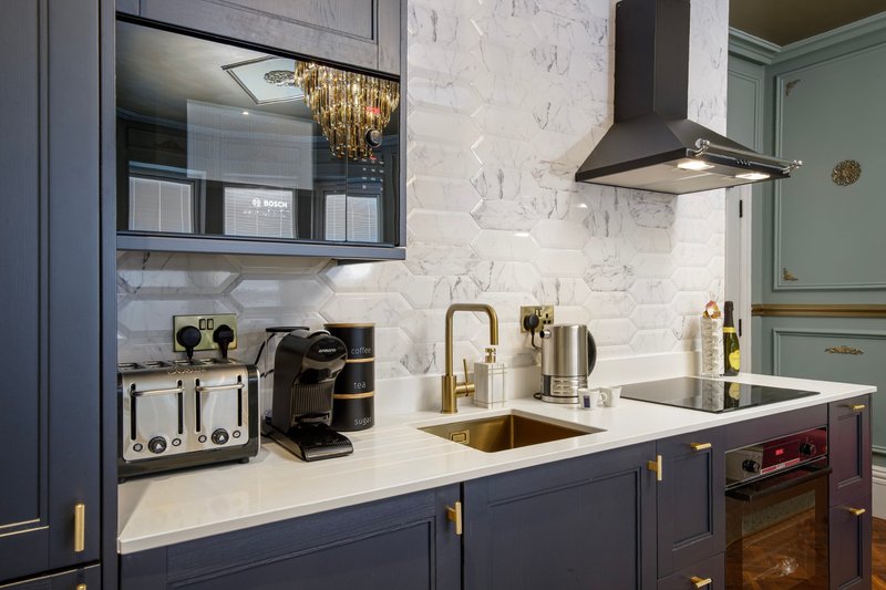 Modern kitchen with white marble backsplash, dark blue cabinetry, gold fixtures and appliances