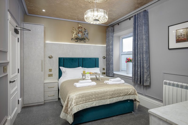 Modern bedroom with teal upholstered bed, white bedside tables, chandelier and blue curtains