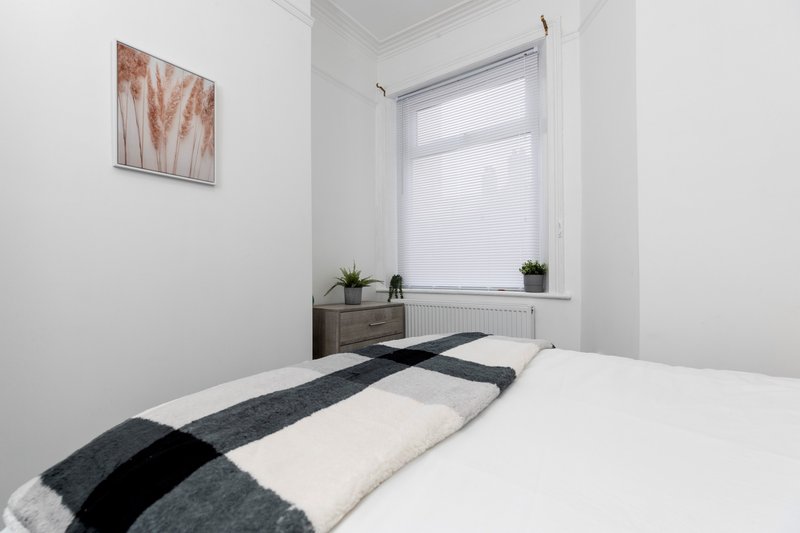 Bright bedroom with double bed, striped throw blanket, small dresser and window with blinds