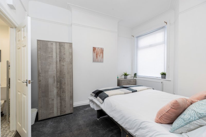Bright bedroom with single bed, wardrobe, window, and potted plants on radiator shelf