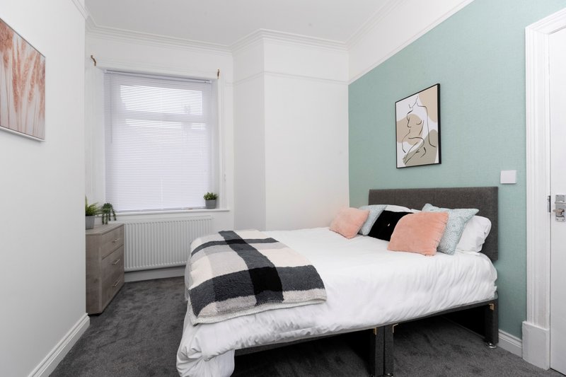 Bedroom with double bed, teal accent wall, window, and minimalist decor
