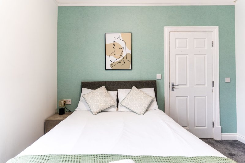 Bedroom with double bed, turquoise accent wall, framed artwork and white door