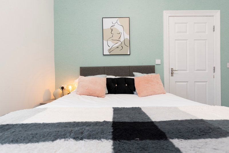 Modern bedroom with double bed, pink cushions, framed line art above headboard, white door