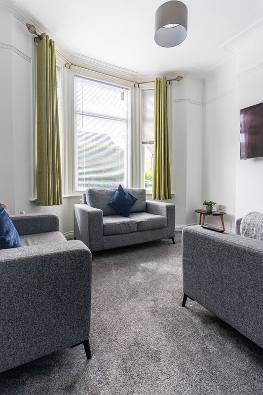 Bright living room with grey upholstered seating, bay window with green curtains, and ceiling light fixture