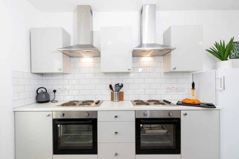 Modern white kitchen with dual ovens, range hoods, subway tile backsplash and stainless steel appliances