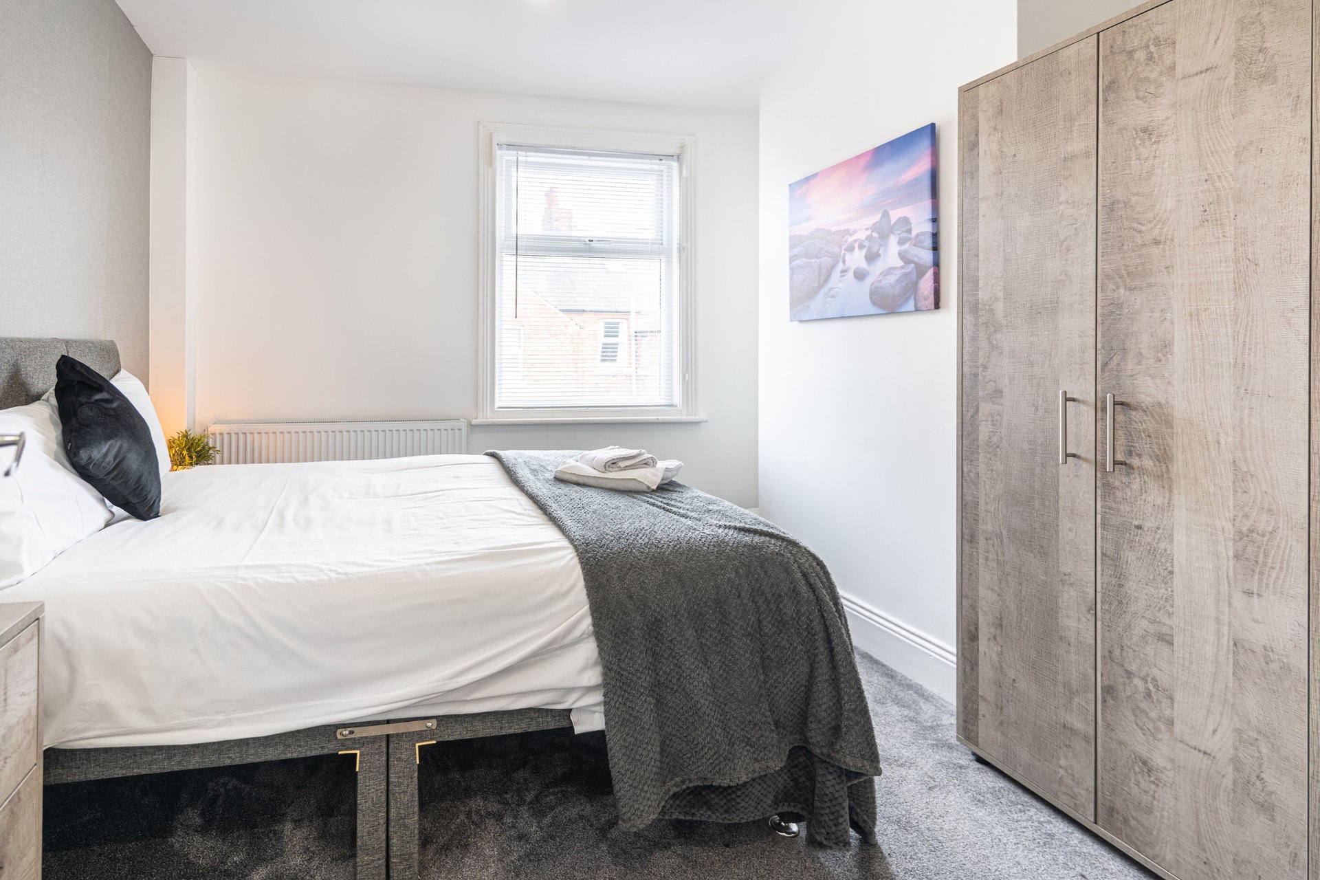 Bright bedroom with double bed, grey throw, wooden wardrobe and window view