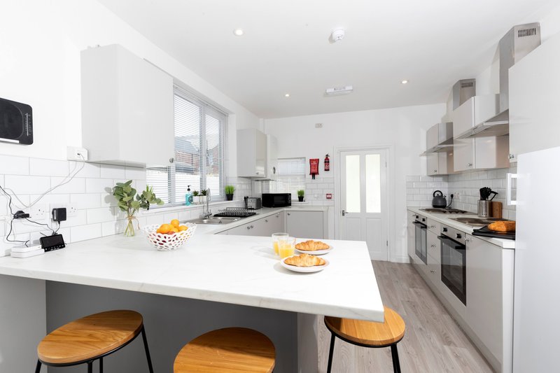Modern white kitchen with island, wooden bar stools, stainless steel appliances and natural light