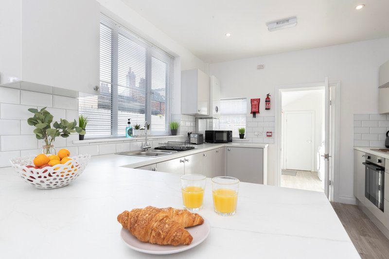 Modern white kitchen with island, croissants, orange juice and fresh plants on countertop