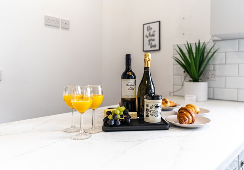 Modern kitchen island with wine bottles, glasses, fresh fruit, croissants and green plant
