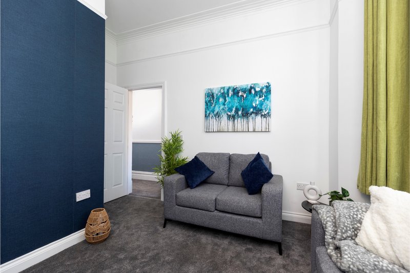 Modern living room with gray sofa, blue abstract wall art, dark blue accent wall, and green curtains