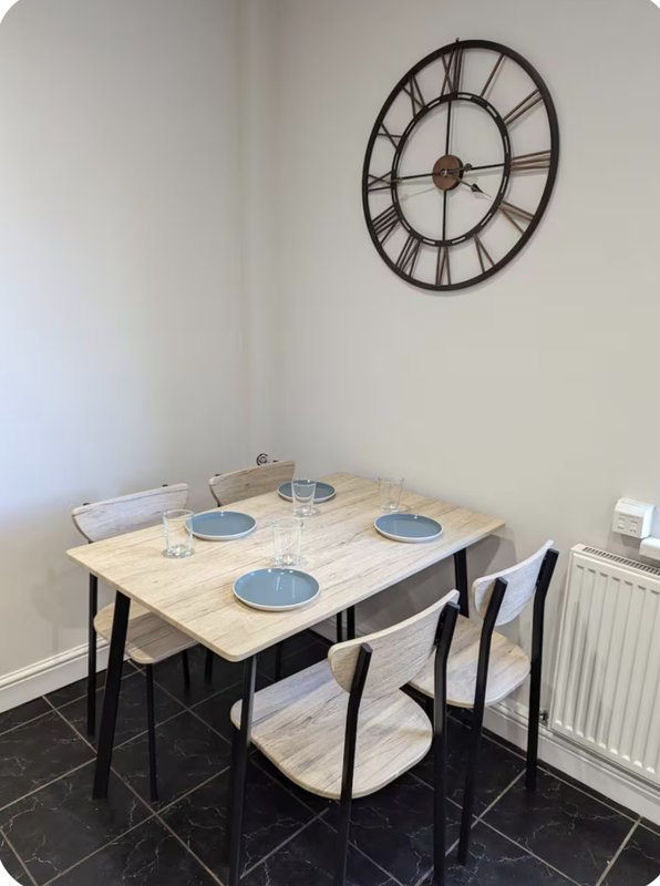 Dining table with four chairs, place settings, large wall clock, and radiator