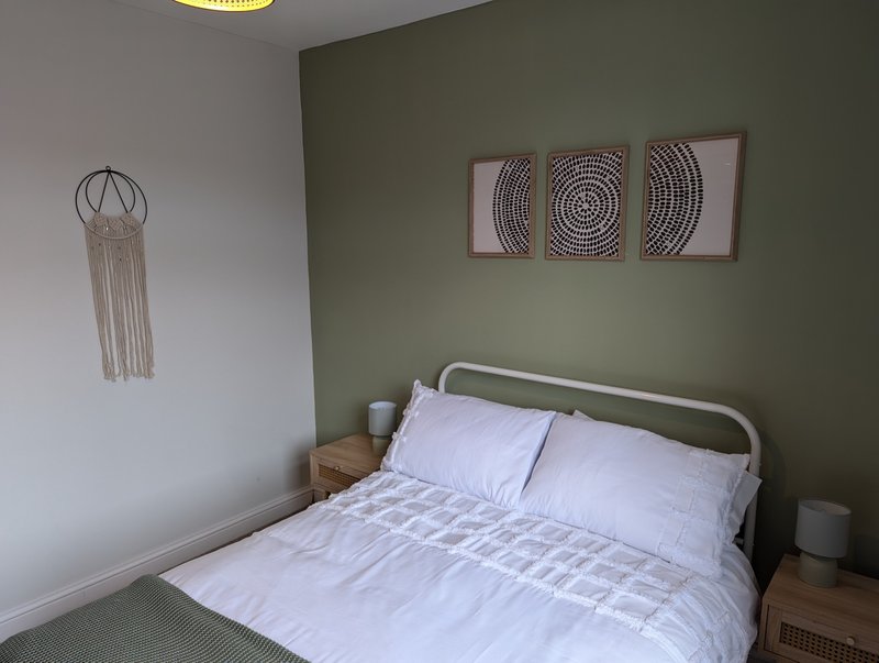 Bedroom with double bed, white bedding, green accent wall, wall art and wind chime
