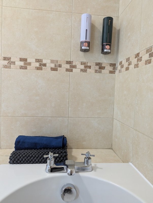 Bathroom sink with tiled walls, towel dispenser and rolled towels on counter