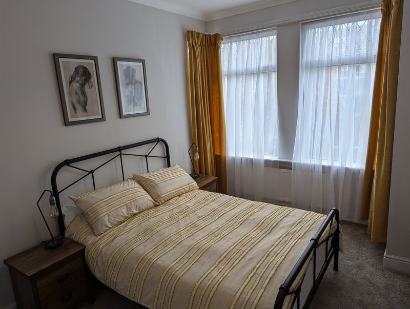 Bedroom with metal-framed bed, striped bedding, wooden nightstand, framed wall art, and gold curtains