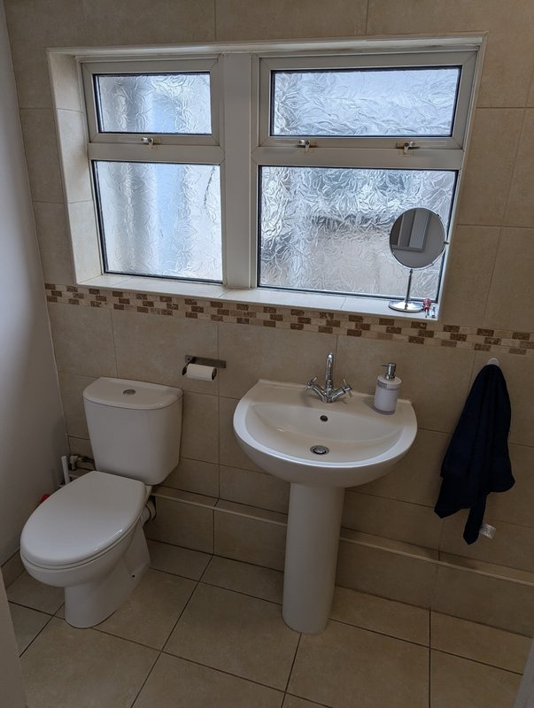 Bathroom with toilet, pedestal sink, window, and tiled walls with decorative border