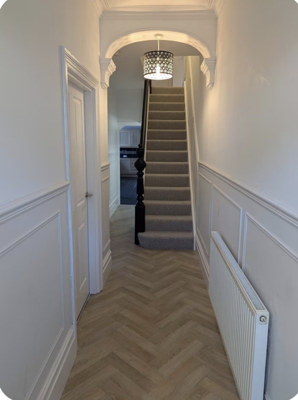 Hallway with herringbone wooden floor, white panelled walls, staircase and pendant light