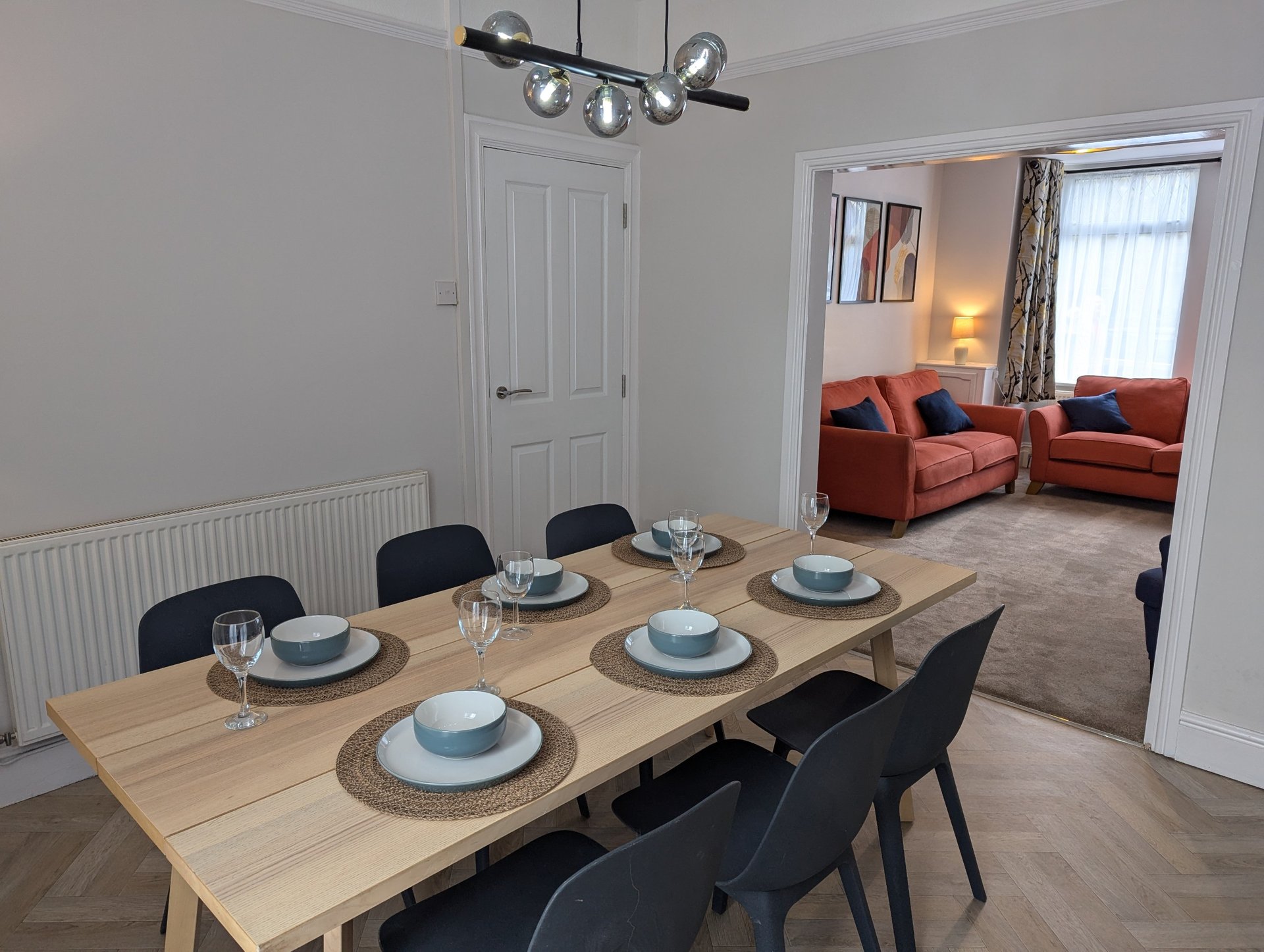 Dining room with wooden table, black chairs, place settings, and view into living room with red sofa