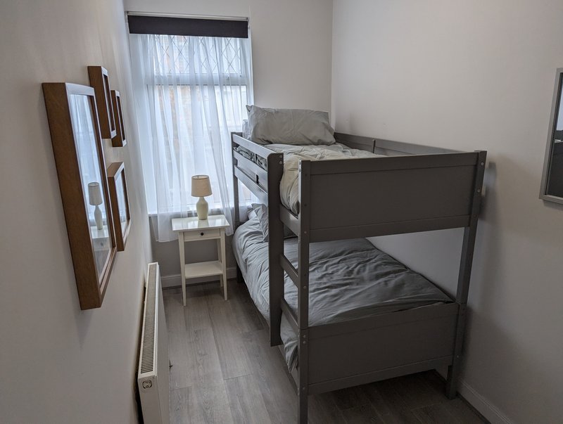Bright bedroom with bunk bed, mirror, side table, lamp and window with curtains