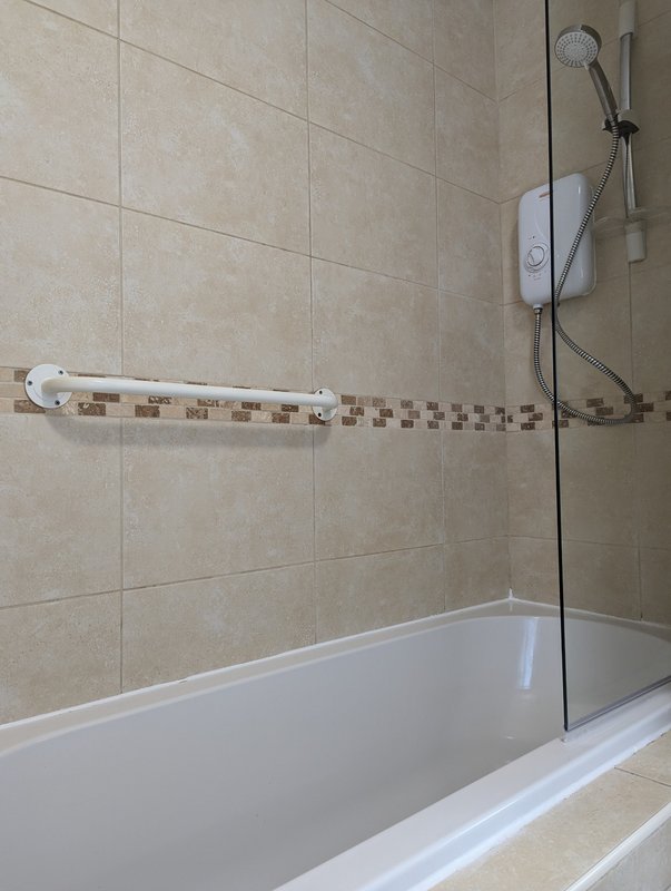 Bathroom with white bathtub, beige tile walls, shower head and towel rail