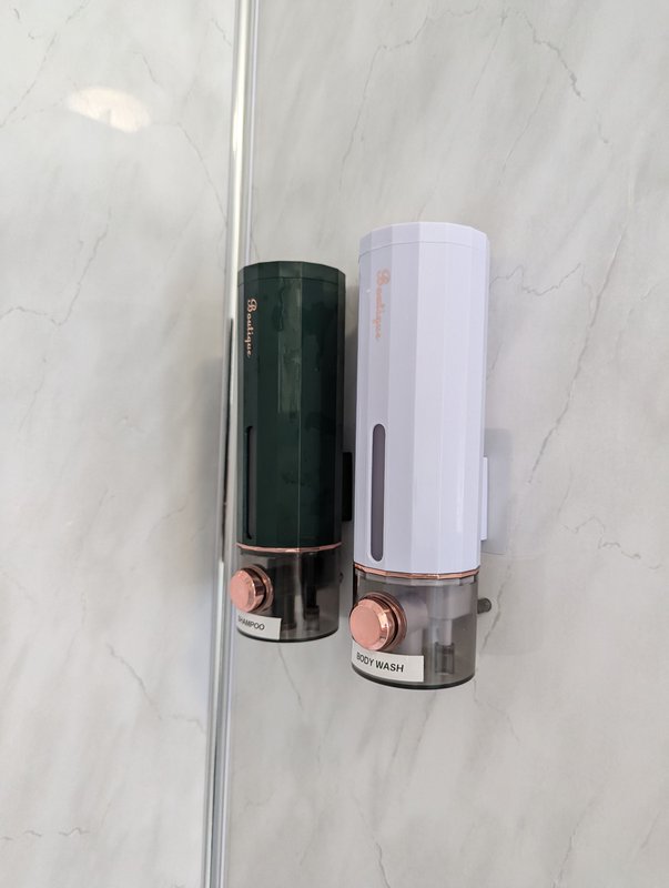 Two wall-mounted soap dispensers on marble tile bathroom wall