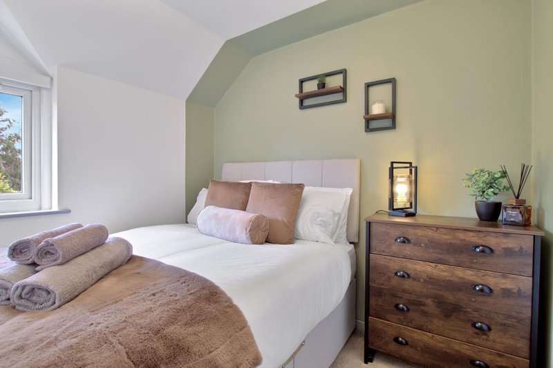 Bedroom with double bed, rolled towels, wooden dresser, and sage green accent wall