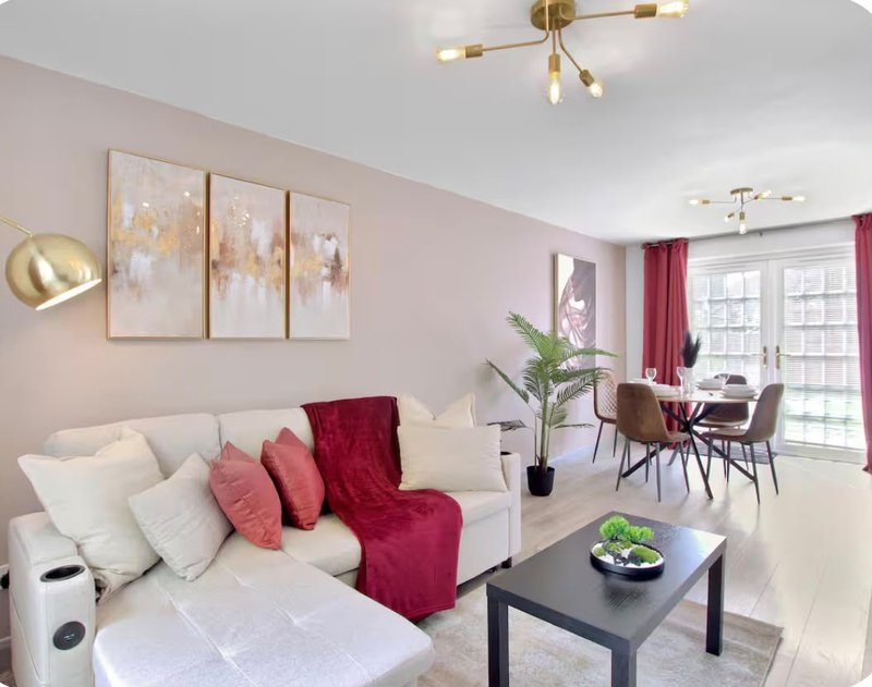 Modern living room with cream sofa, burgundy accents, wall art, and dining area beyond
