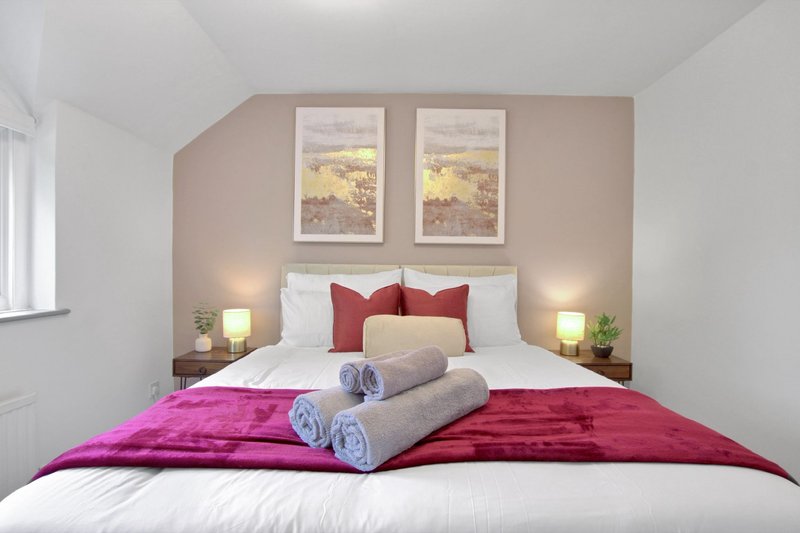 Modern bedroom with double bed, pink and red bedding, framed artwork, and side lamps