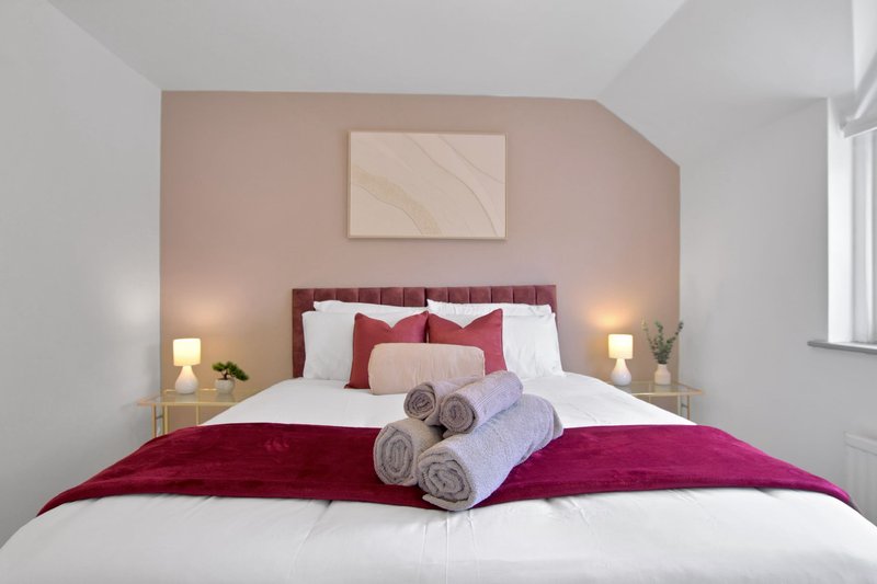 Modern bedroom with burgundy headboard, white bedding, rolled towels, and pink accent wall