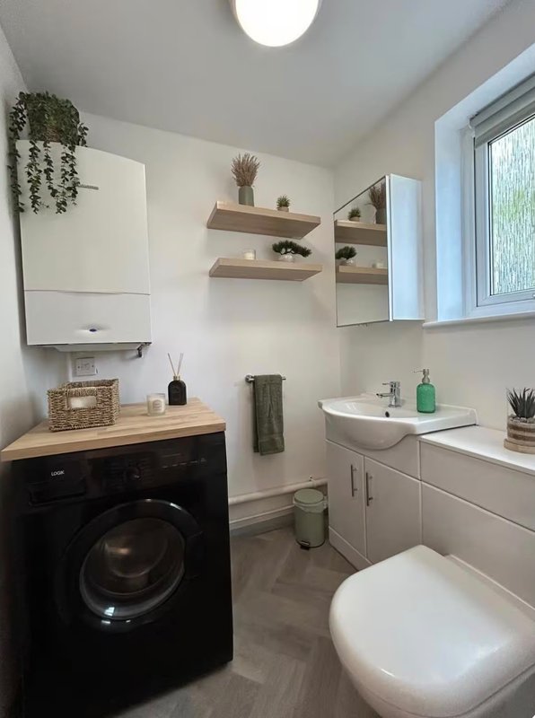 Modern bathroom with washing machine, toilet, sink, shelving and window