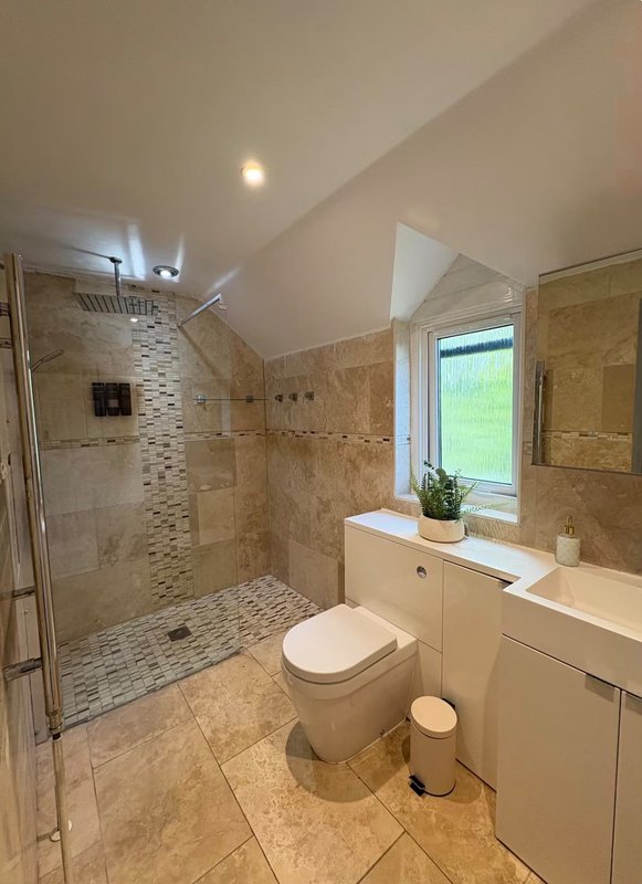 Modern bathroom with walk-in shower, toilet, vanity sink and window overlooking garden