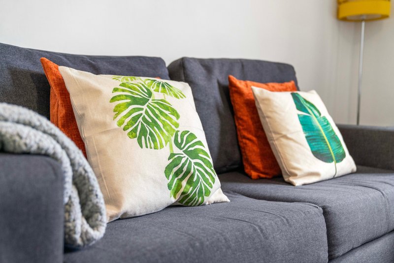 Gray sofa with decorative cushions featuring tropical leaf prints and throws